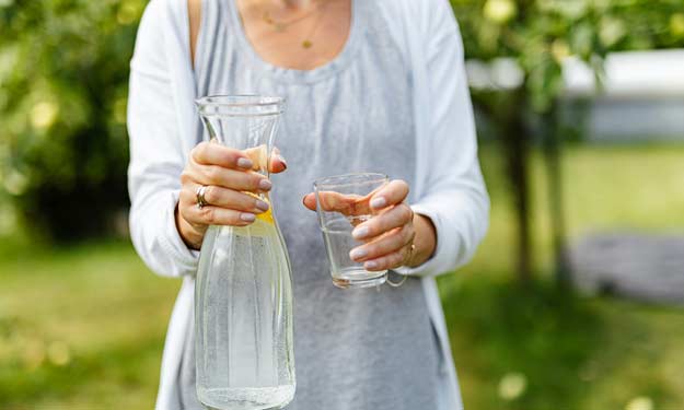 Woman Holding Glass and Pitcher Getting Ready to Do a Herbal Liver Detox.