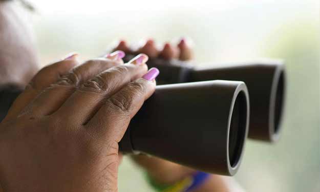 Woman Looking Through Binoculars to Explore the Pages of The Inquisitive Enthusiast Website